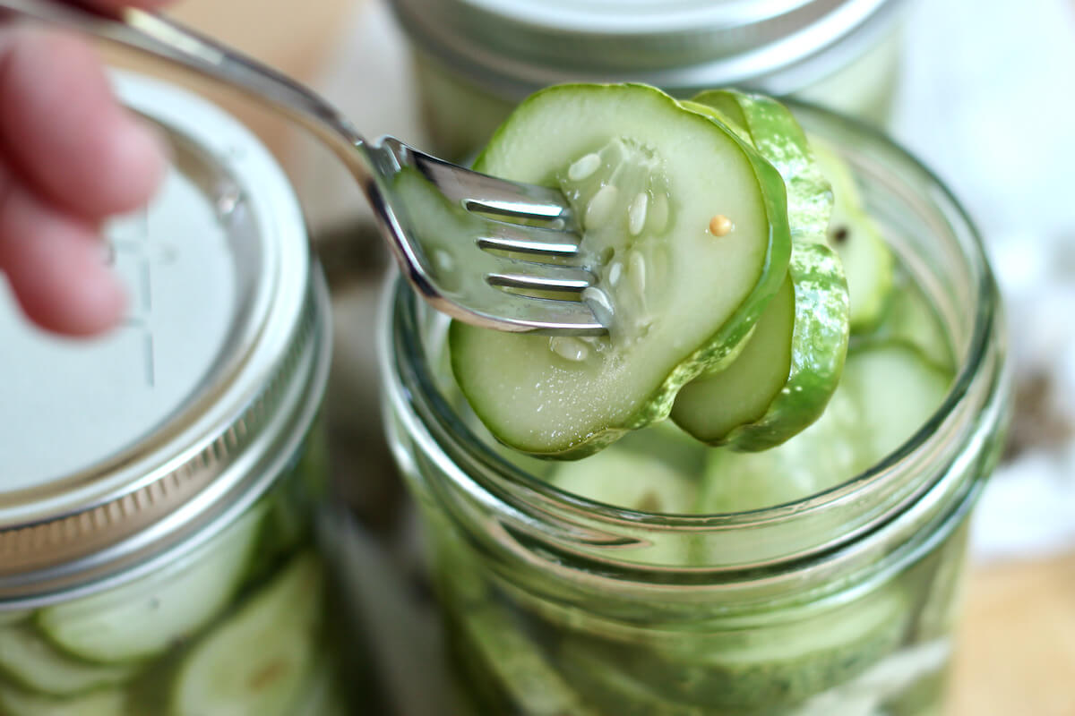 A fork removing three refrigerator dill pickles from an open jar.