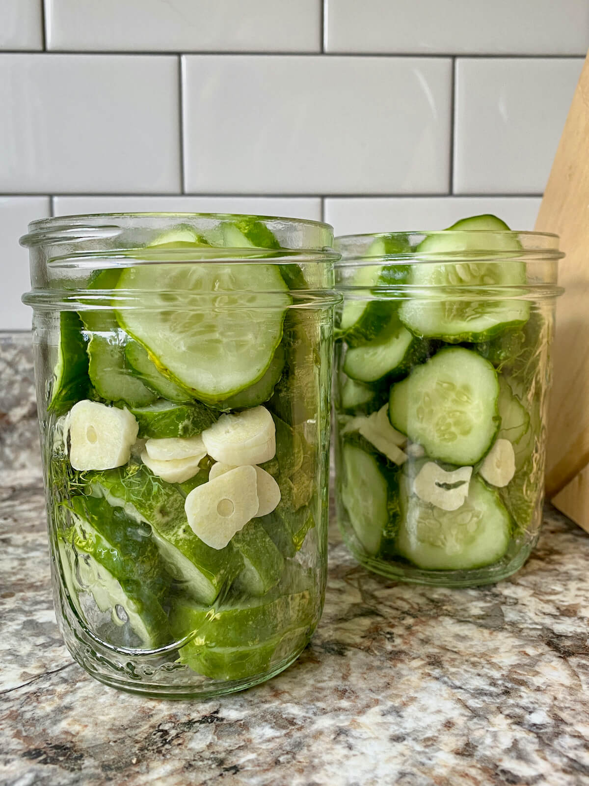 Glass mason jars filled with sliced cucumbers, garlic, and dill.