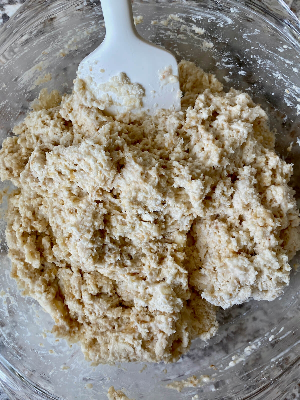 The dough roughly mixed with a rubber spatula in a glass mixing bowl.