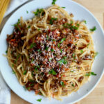 A plate of linguine bolognese garnished with fresh parsley and grated parmesan cheese.