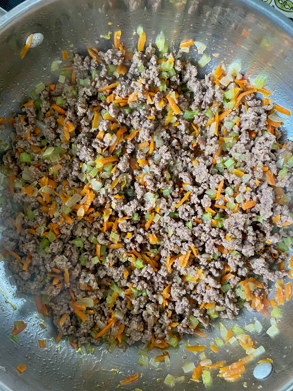 Cooked ground beef, onions, celery, and carrots in a stainless steel pot.