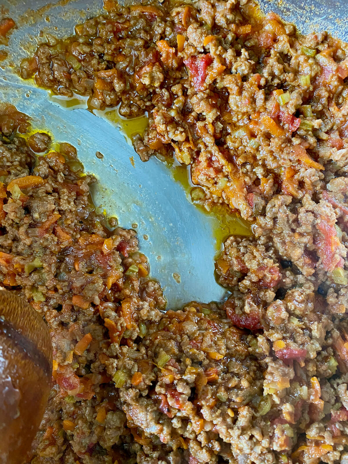 A wooden spoon dragging through the bolognese sauce to show the thickness.