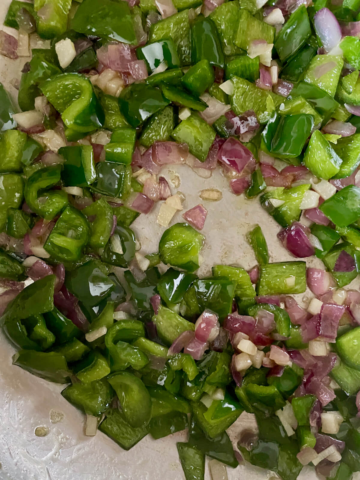 Poblano peppers, jalapeño peppers, red onion, and garlic sautéing in olive oil in a stainless steel pot.