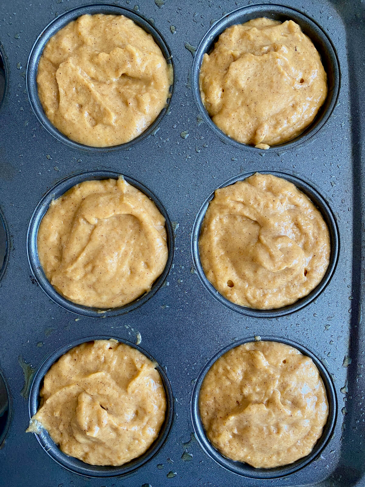 Six muffin pan wells filled with sourdough pumpkin muffin batter.