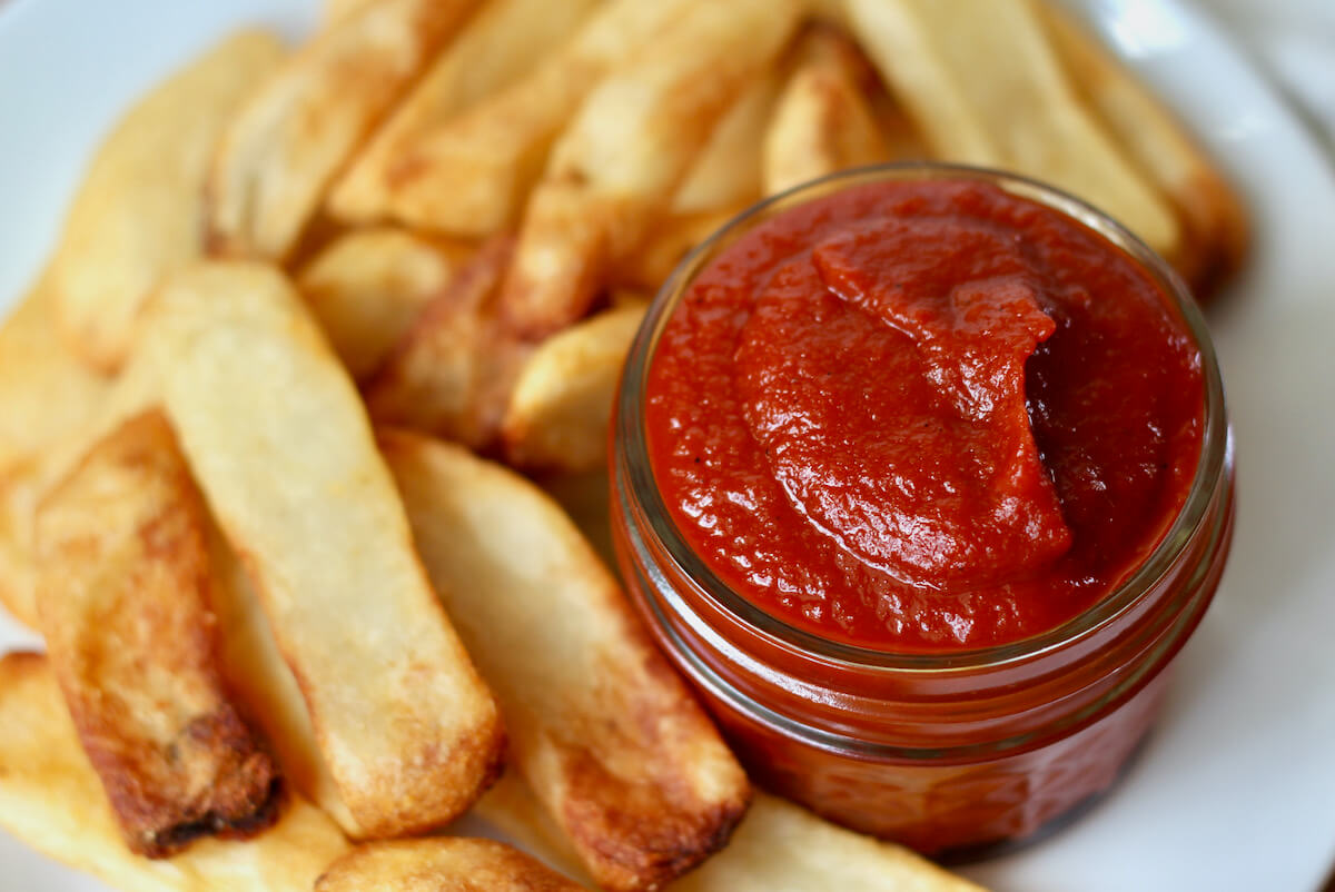 A small glass jar of homemade ketchup on a plate of fries.