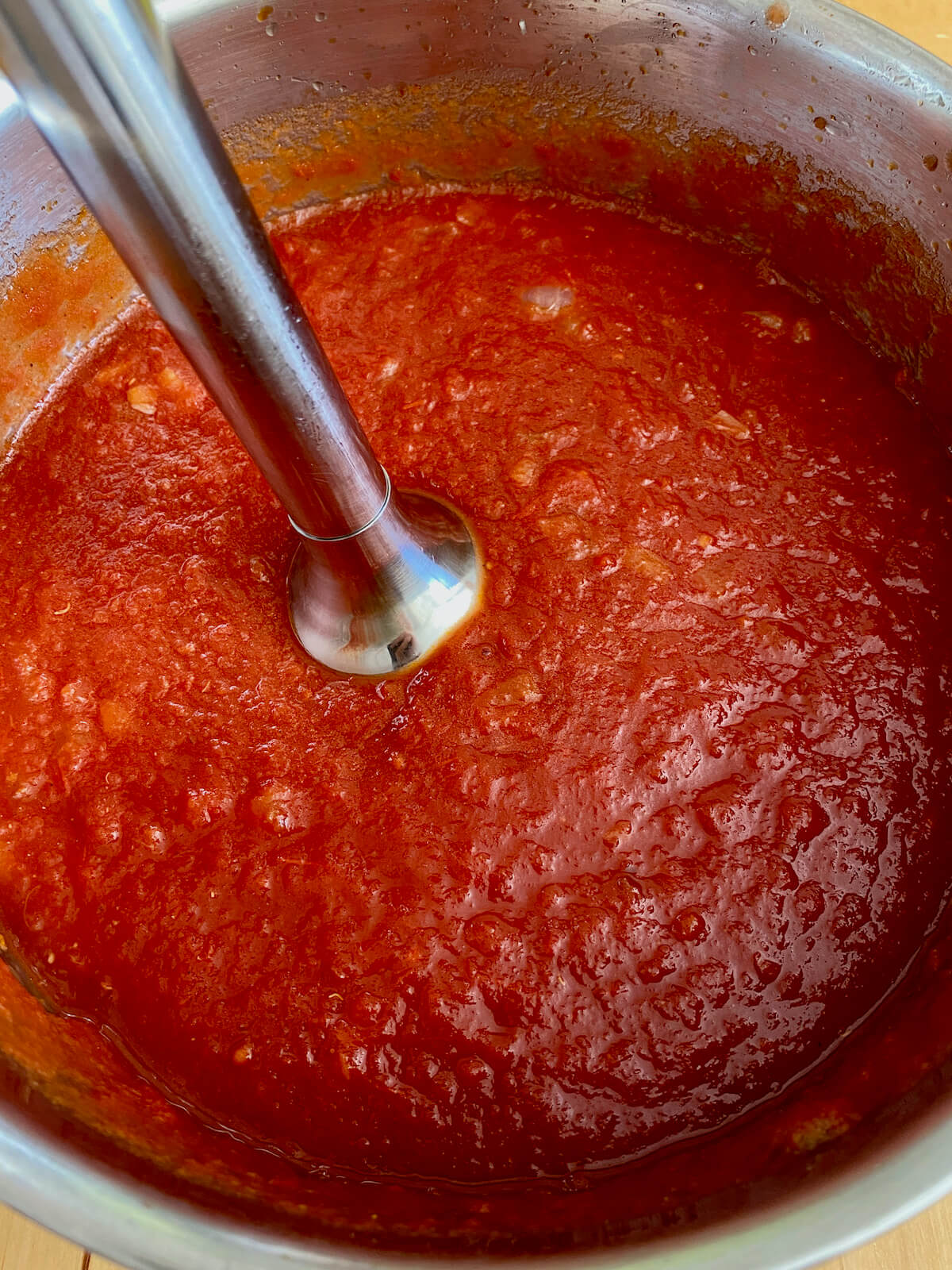 An immersion blender blending the crushed tomatoes and aromatics together.
