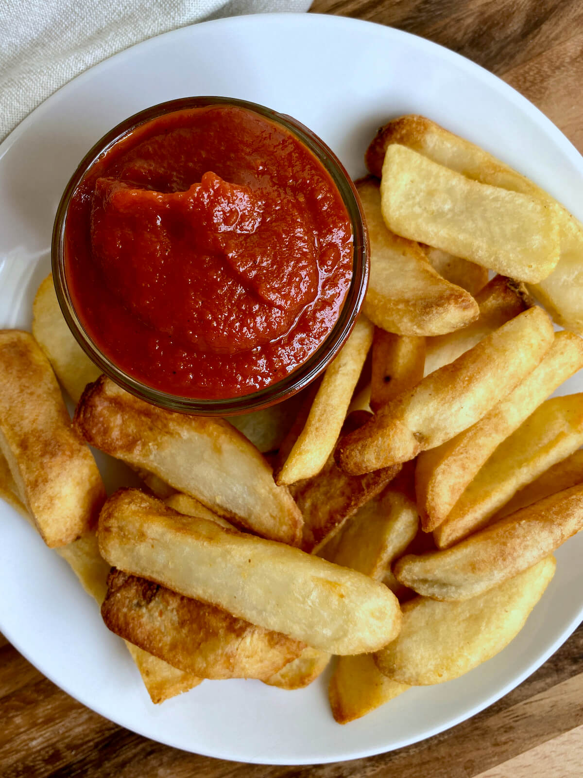 A jar of homemade ketchup on a plate of steak fries.