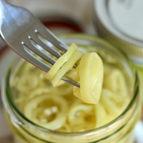 A fork holding a few slices of pickled banana peppers above a jar.