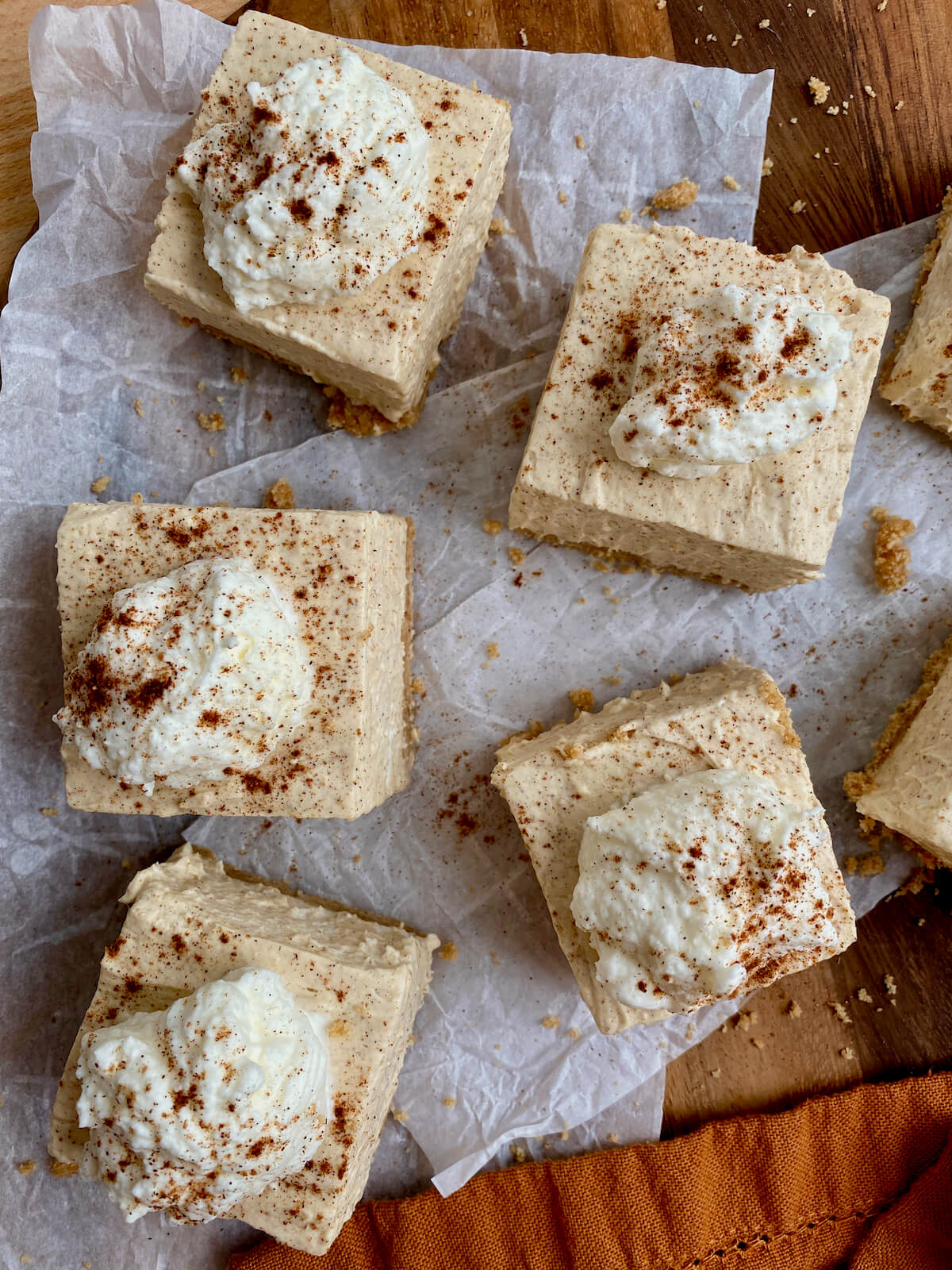 No-bake pumpkin cheesecake bars garnished with a dollop of whipped cream and spices and cut into squares.