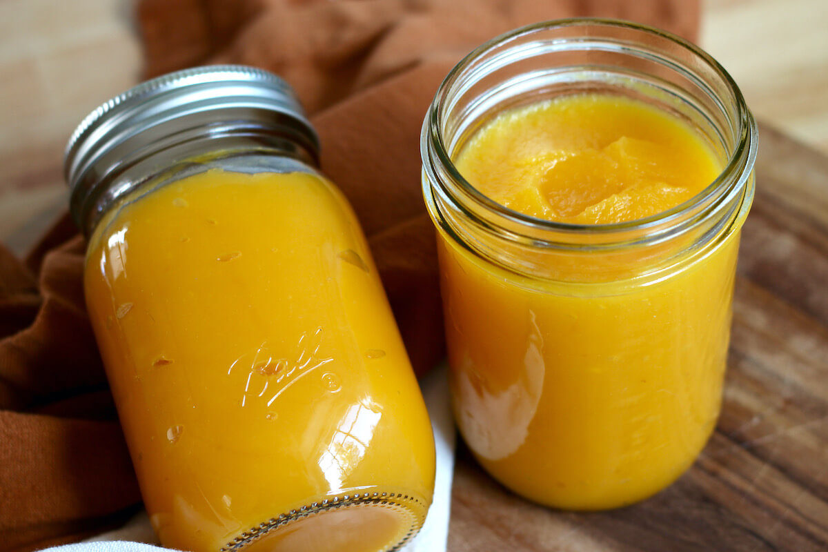 Two jars of roasted pumpkin puree. The left jar is sealed and laying on its side. The jar on the right is open and standing upright.