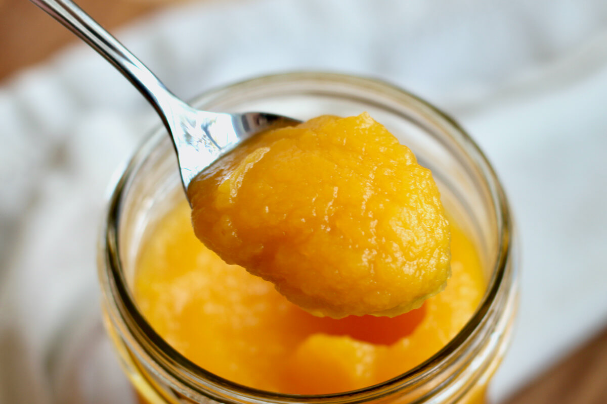 A spoonful of homemade roasted pumpkin puree being held above a jar.