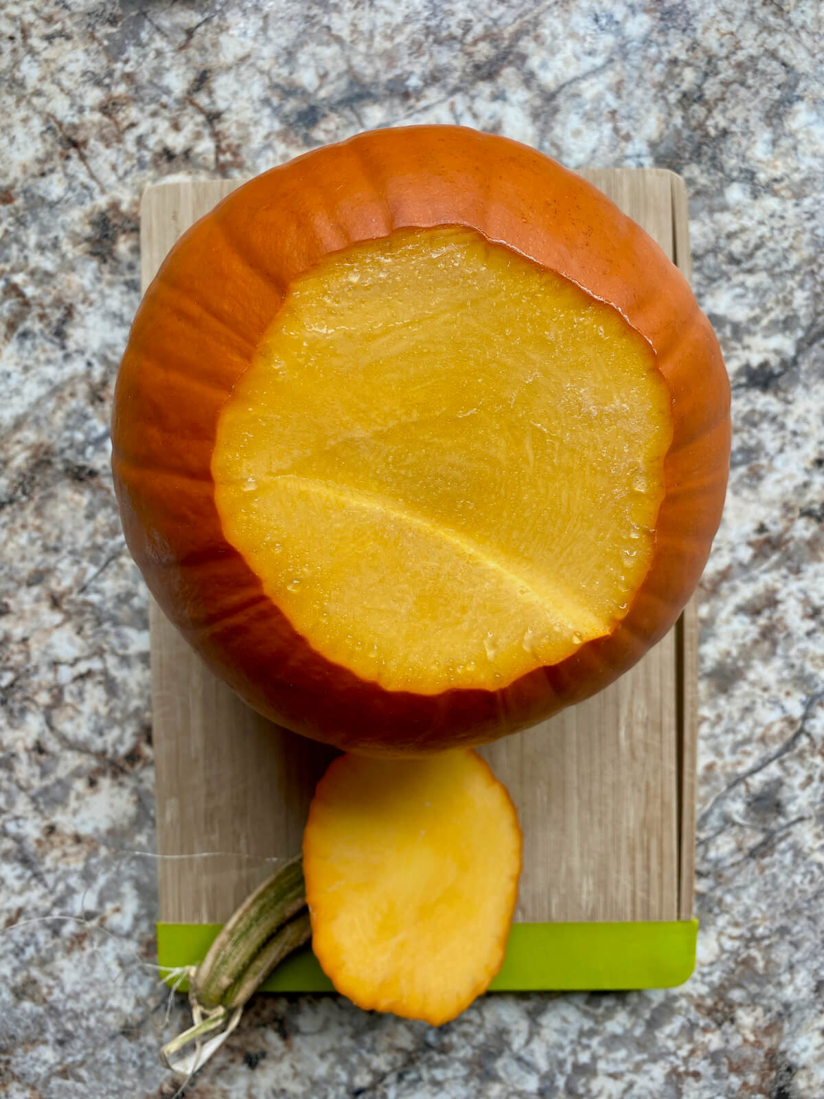 A sugar pumpkin with the stem sliced off on a small cutting board.