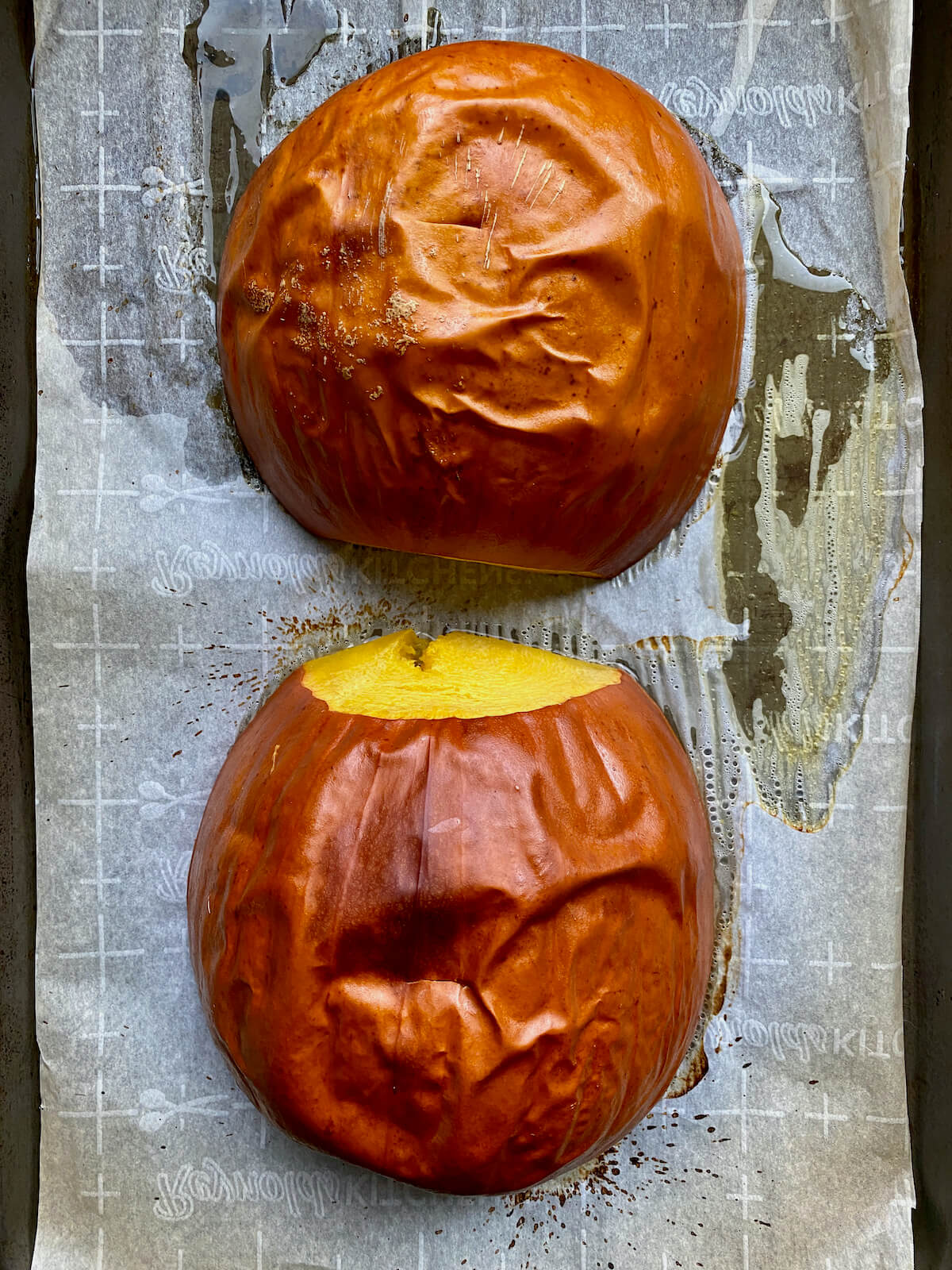 Two roasted pumpkin halves laying cut side down on a parchment-lined baking sheet.