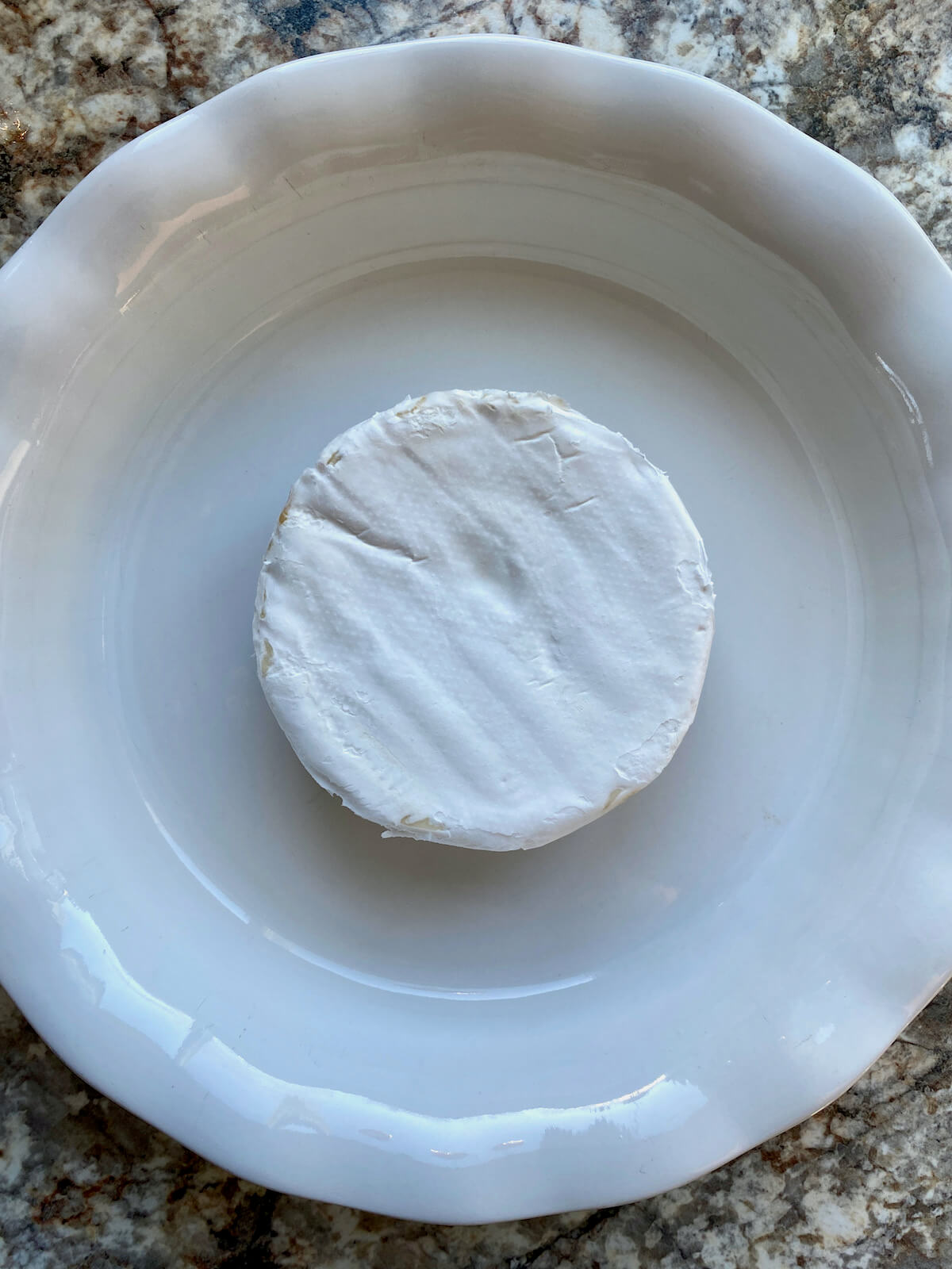 A wheel of Brie cheese in a white pie plate.