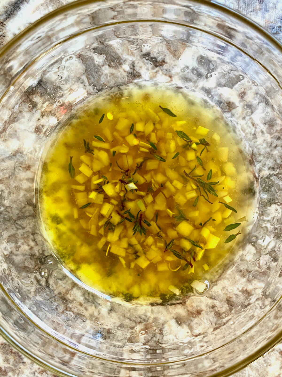 Olive oil, honey, minced garlic, and fresh thyme leaves mixed together in a small glass mixing bowl.