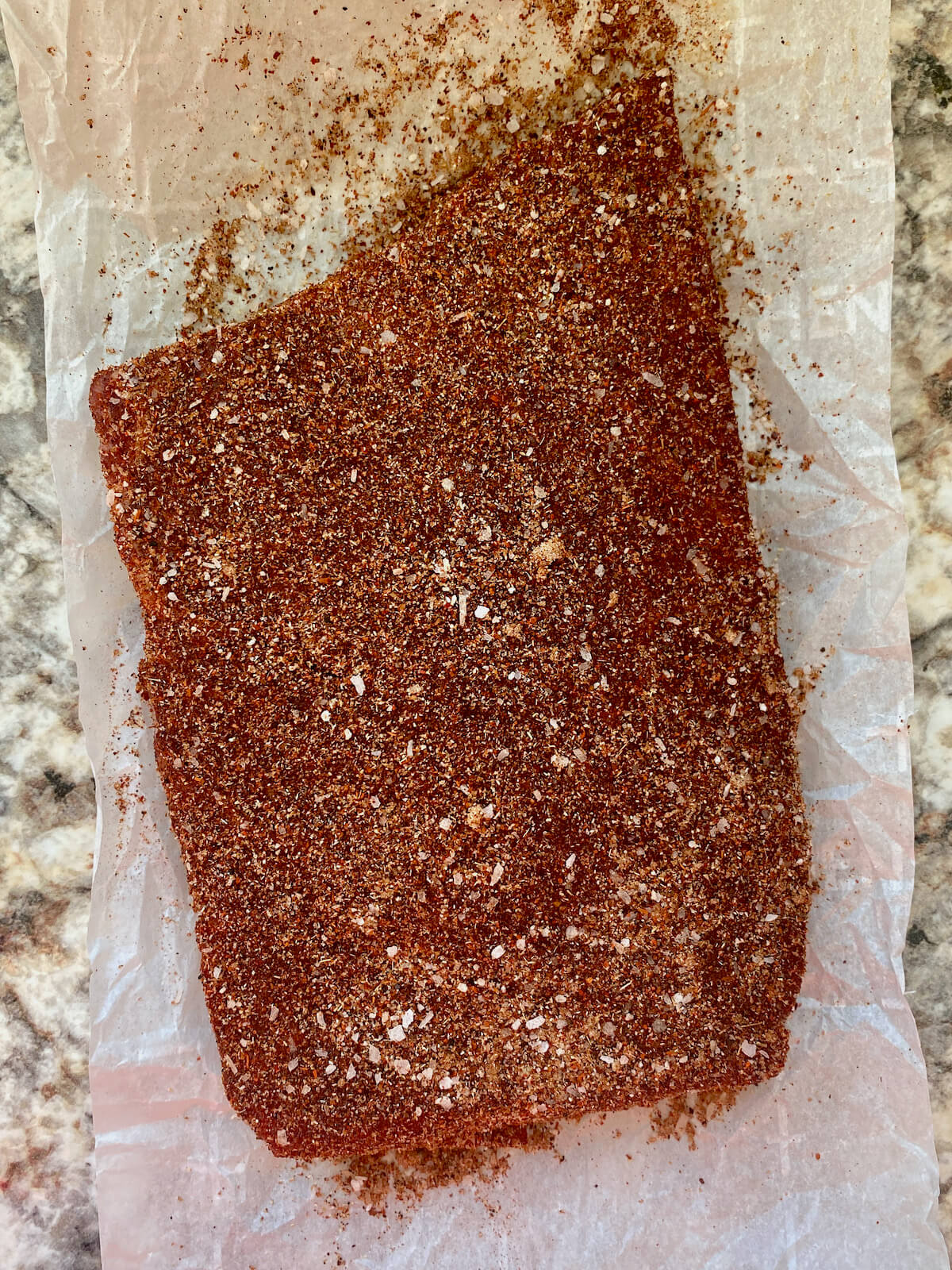 A piece of raw beef coated in fajita seasoning on a piece of parchment paper.