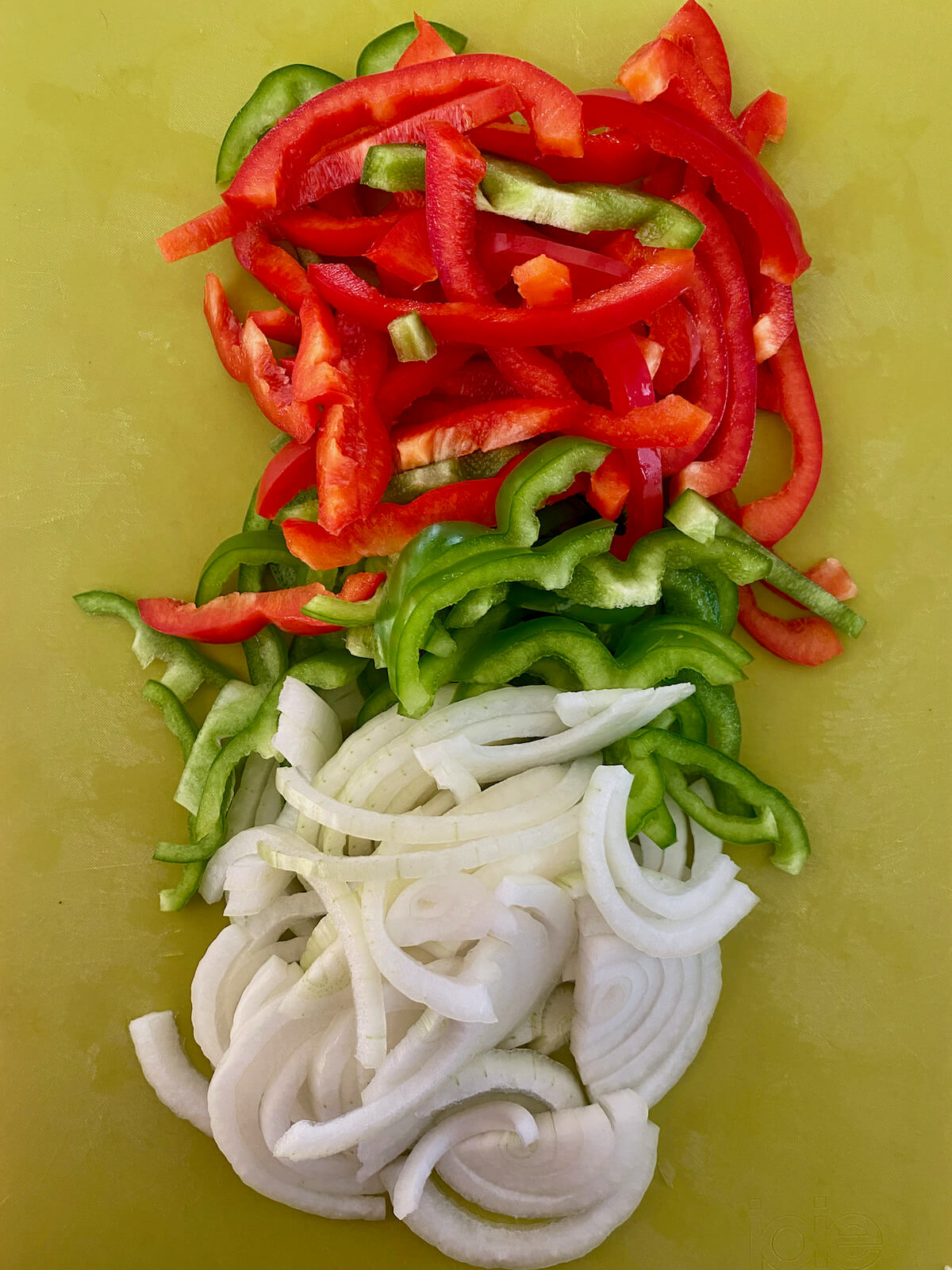 Sliced onion, red bell pepper, and green bell pepper on a green cutting board.