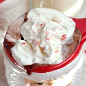 A Santa mug filled with peppermint hot chocolate topped with whipped cream and crushed candy cane.