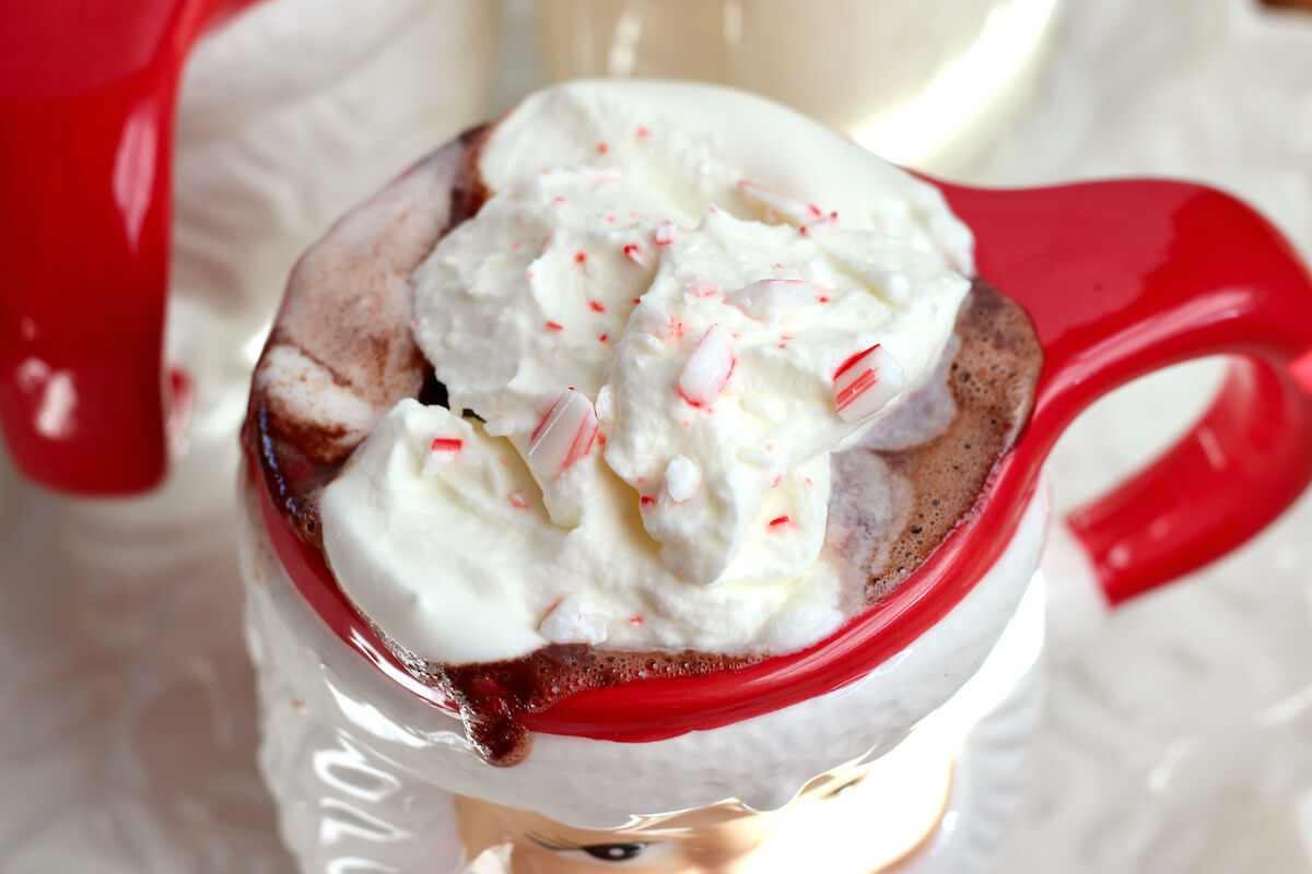 A Santa mug filled with peppermint hot chocolate topped with whipped cream and crushed candy cane.