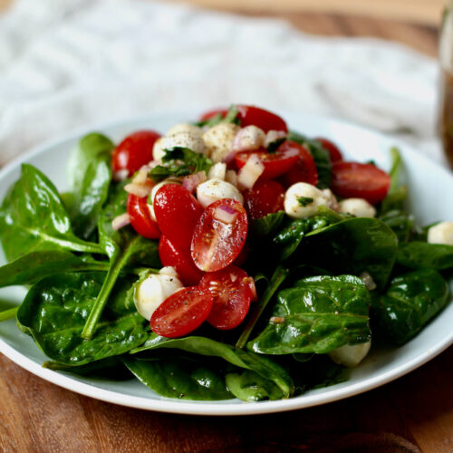 A small white plate of spinach Caprese salad.