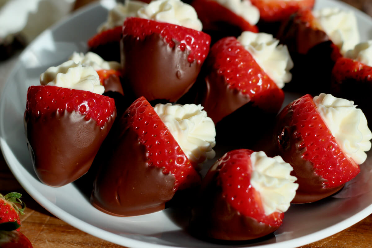 Several chocolate covered strawberries with cheesecake filling on a small white plate.