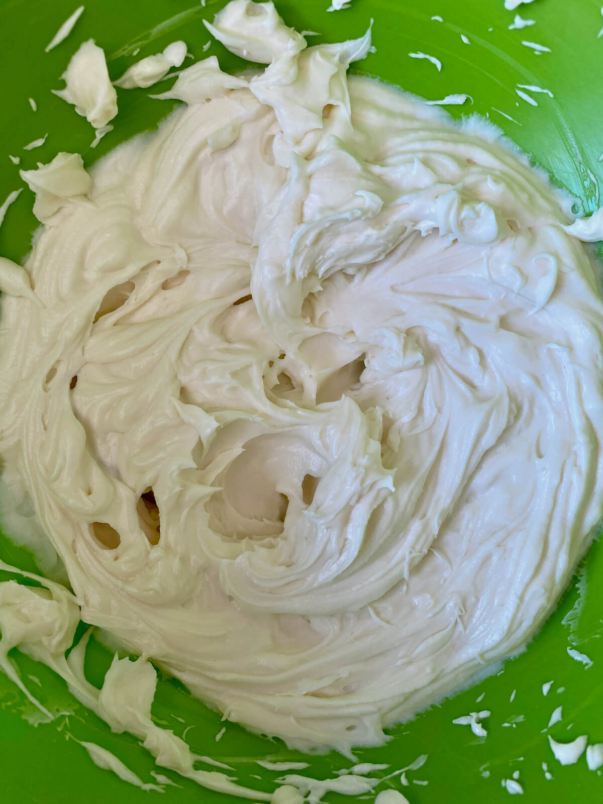 A green mixing bowl filled with whipped cheesecake filling.