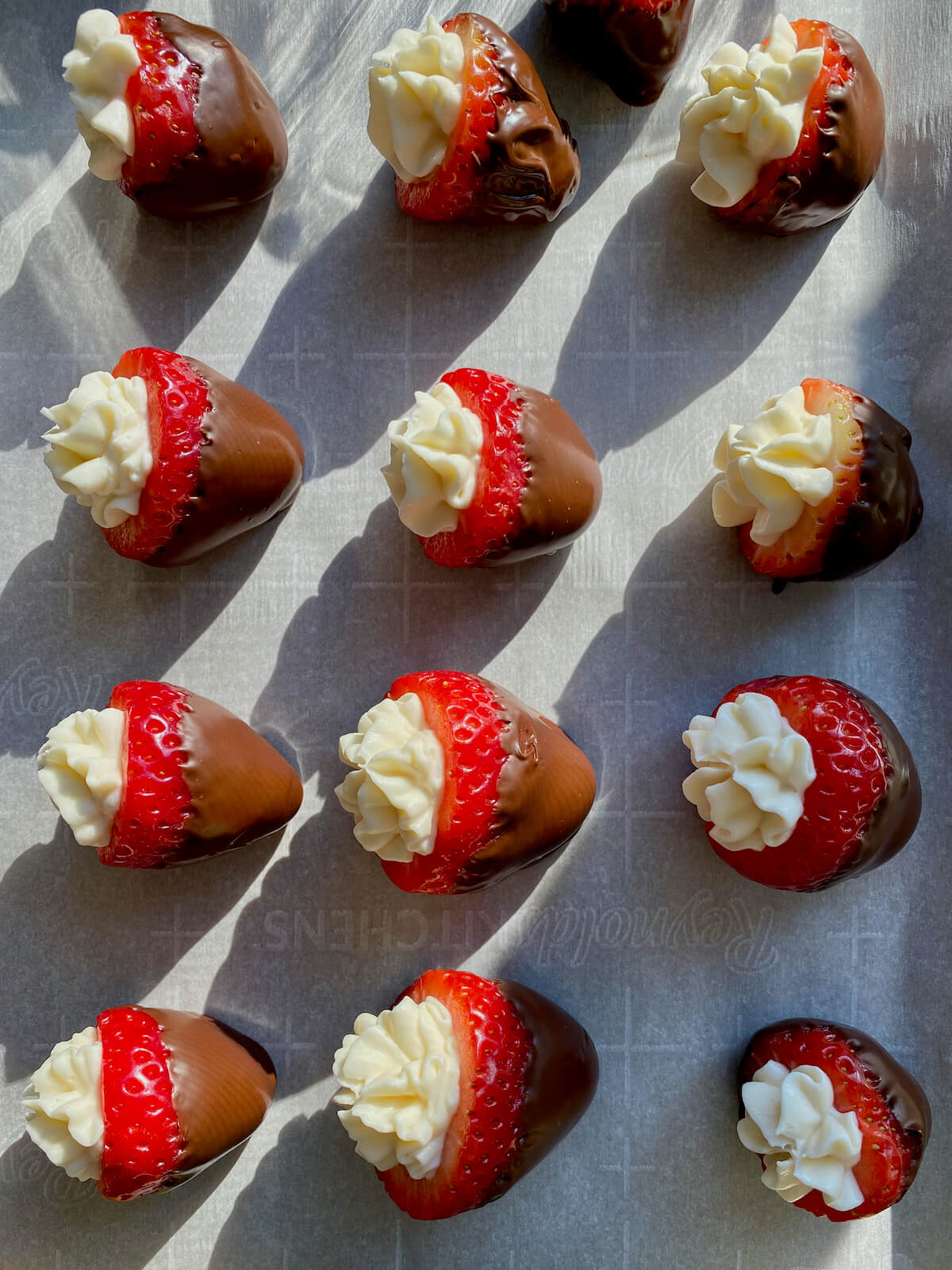 Chocolate covered cheesecake strawberries on a parchment-lined baking sheet.