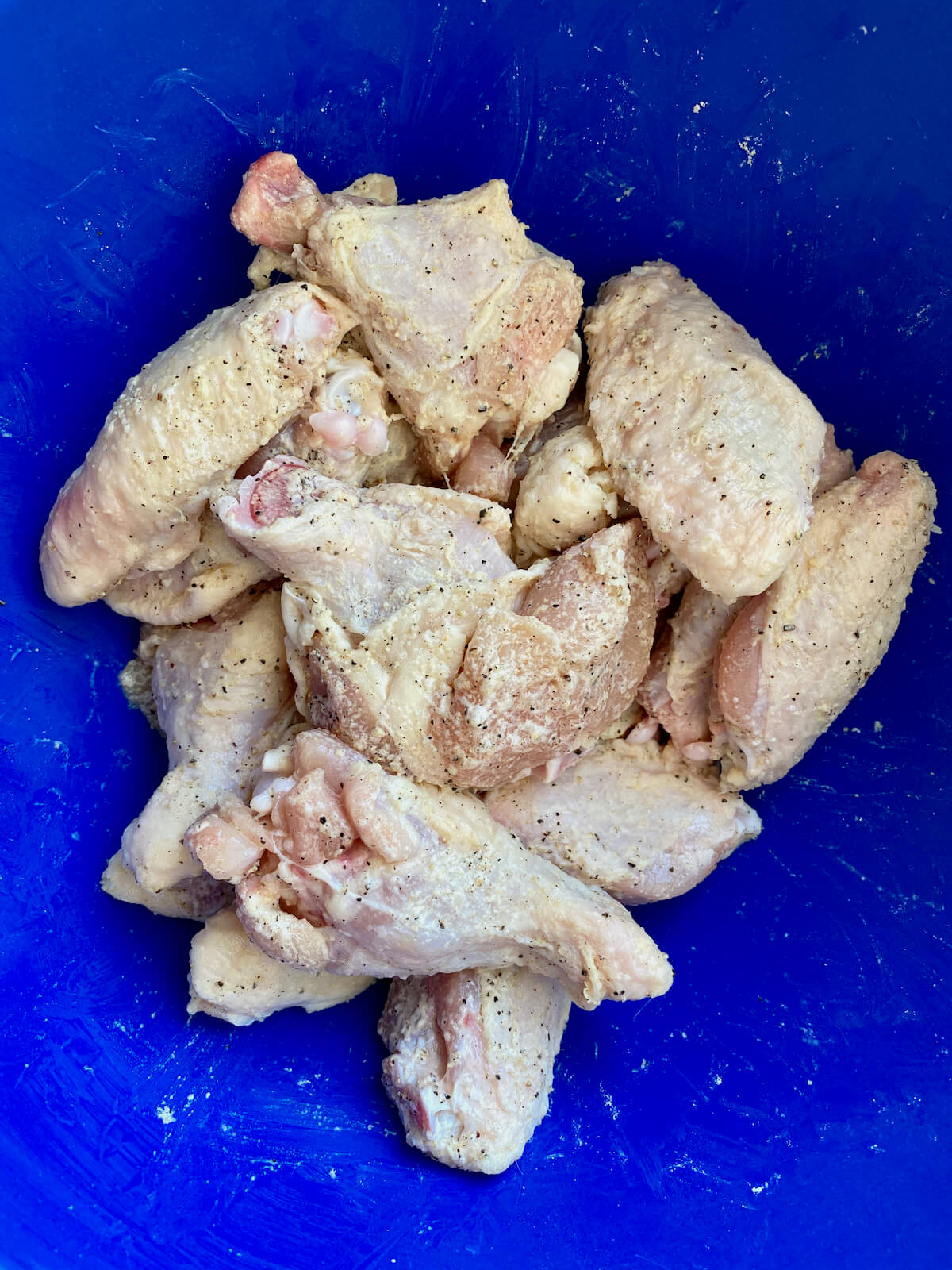 Raw chicken wings tossed with baking powder and seasonings in a blue mixing bowl.
