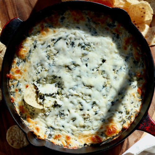A skillet of mayo-free spinach artichoke dip surrounded by tortilla chips.