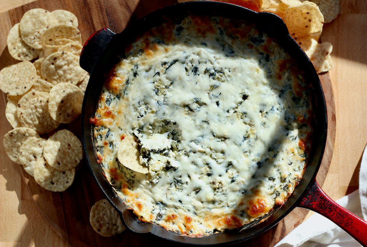 A skillet of mayo-free spinach artichoke dip surrounded by tortilla chips.