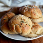 A small plate of sourdough garlic knots garnished with grated parmesan cheese.
