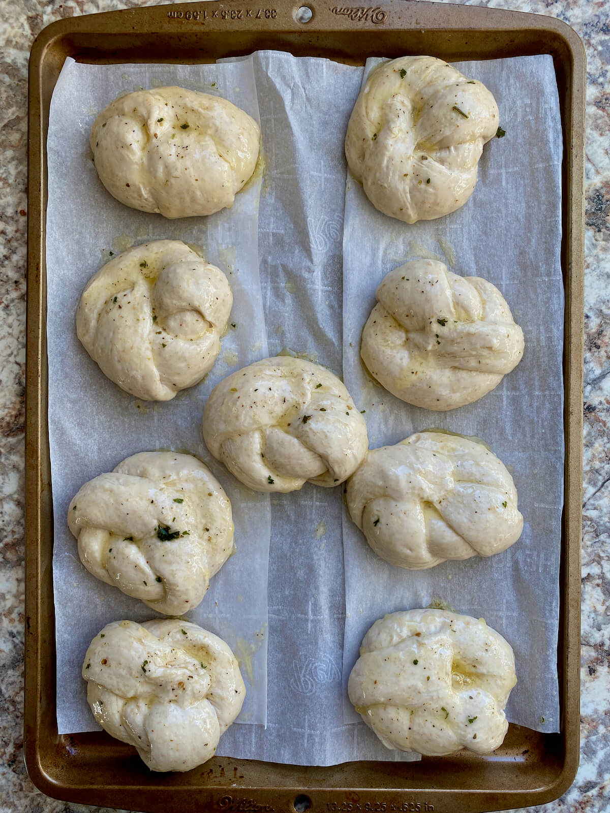 Buttered garlic knots on a parchment-lined baking sheet before baking.
