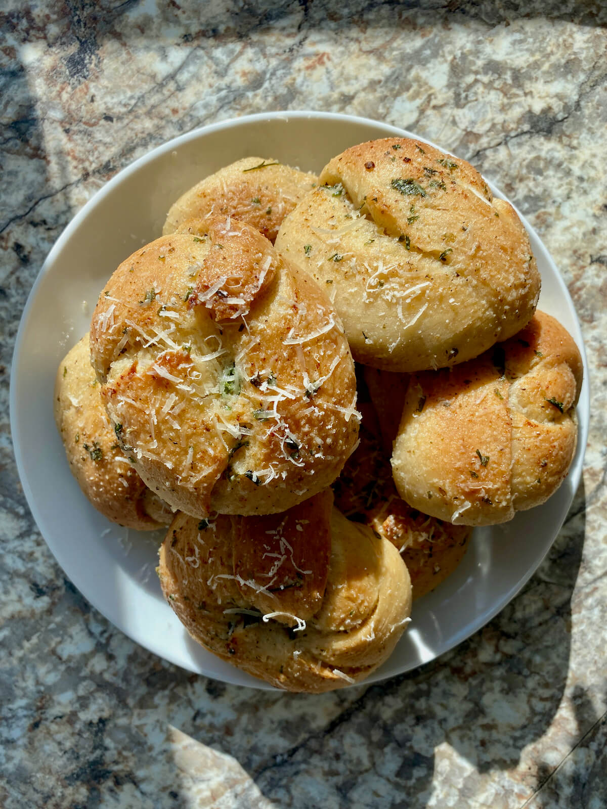 The finished sourdough garlic knots basted with more garlic butter and garnished with parmesan cheese piled on a small plate.