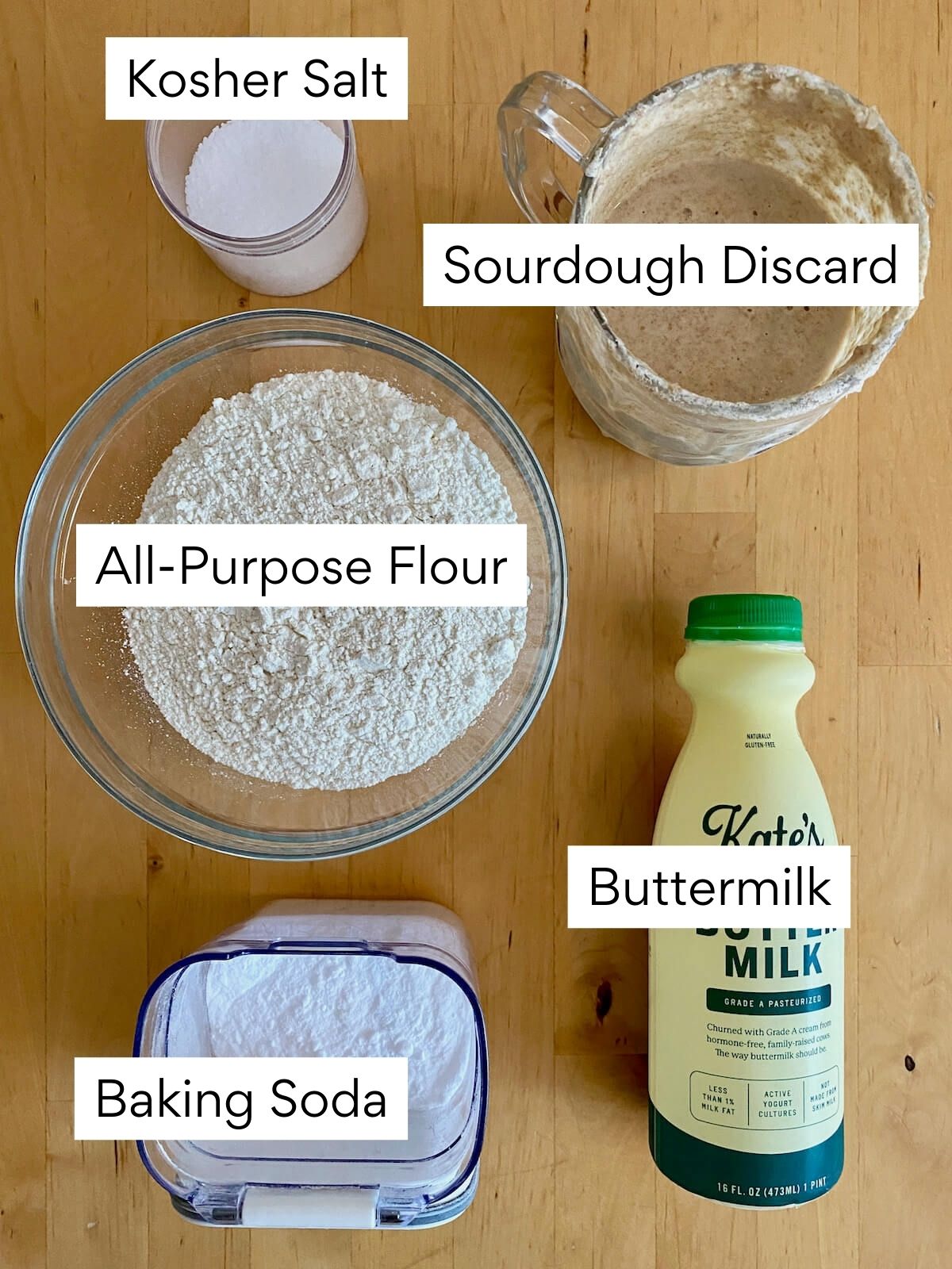 The ingredients to make sourdough Irish soda bread. Each ingredient is labeled with text. They include kosher salt, sourdough discard, all-purpose flour, buttermilk, and baking soda.