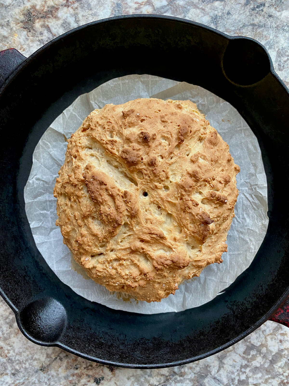A baked sourdough Irish soda bread loaf in a parchment-lined cast iron skillet.