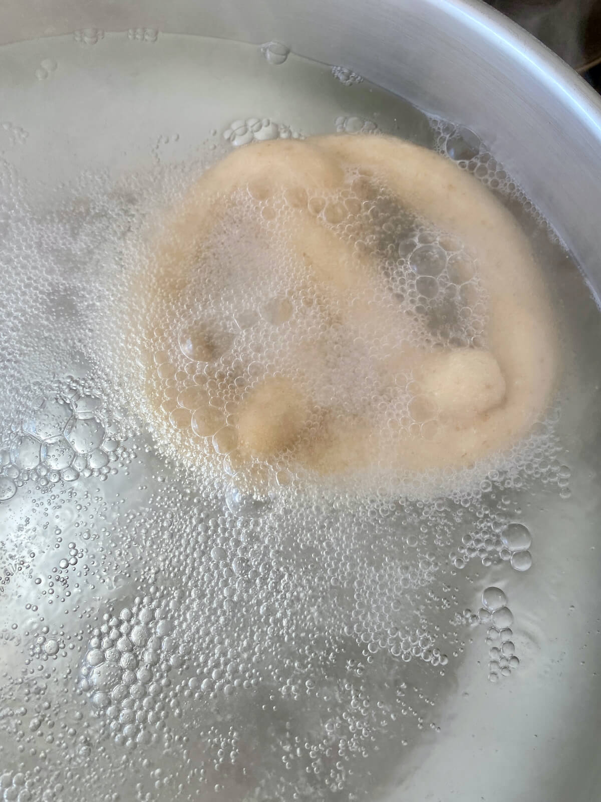 A soft pretzel boiling in a baking soda water bath.