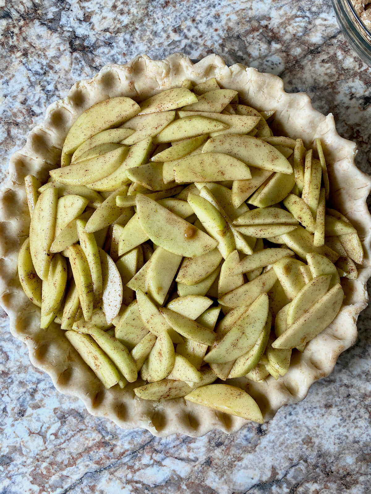 The pie crust filled with the sliced apple filling.