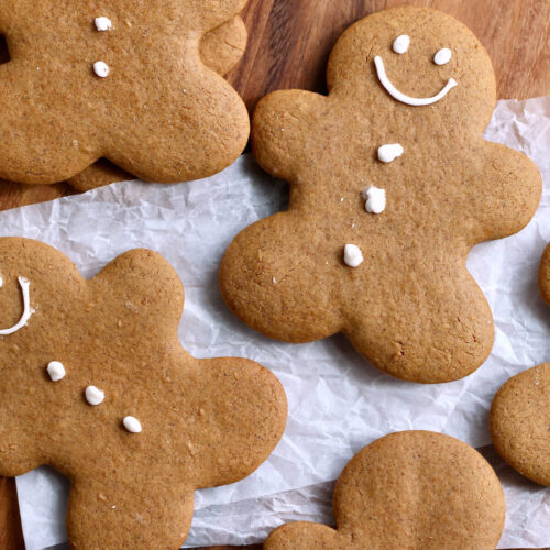 Several sourdough gingerbread cookies on a piece of wrinkled parchment paper on a countertop. The cookies are cut into gingerbread men and have a simple face and three button design on them.