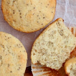 Sourdough lemon poppyseed muffins on a piece of wrinkled parchment paper. One of the muffins is split in half, laying on the paper liner.