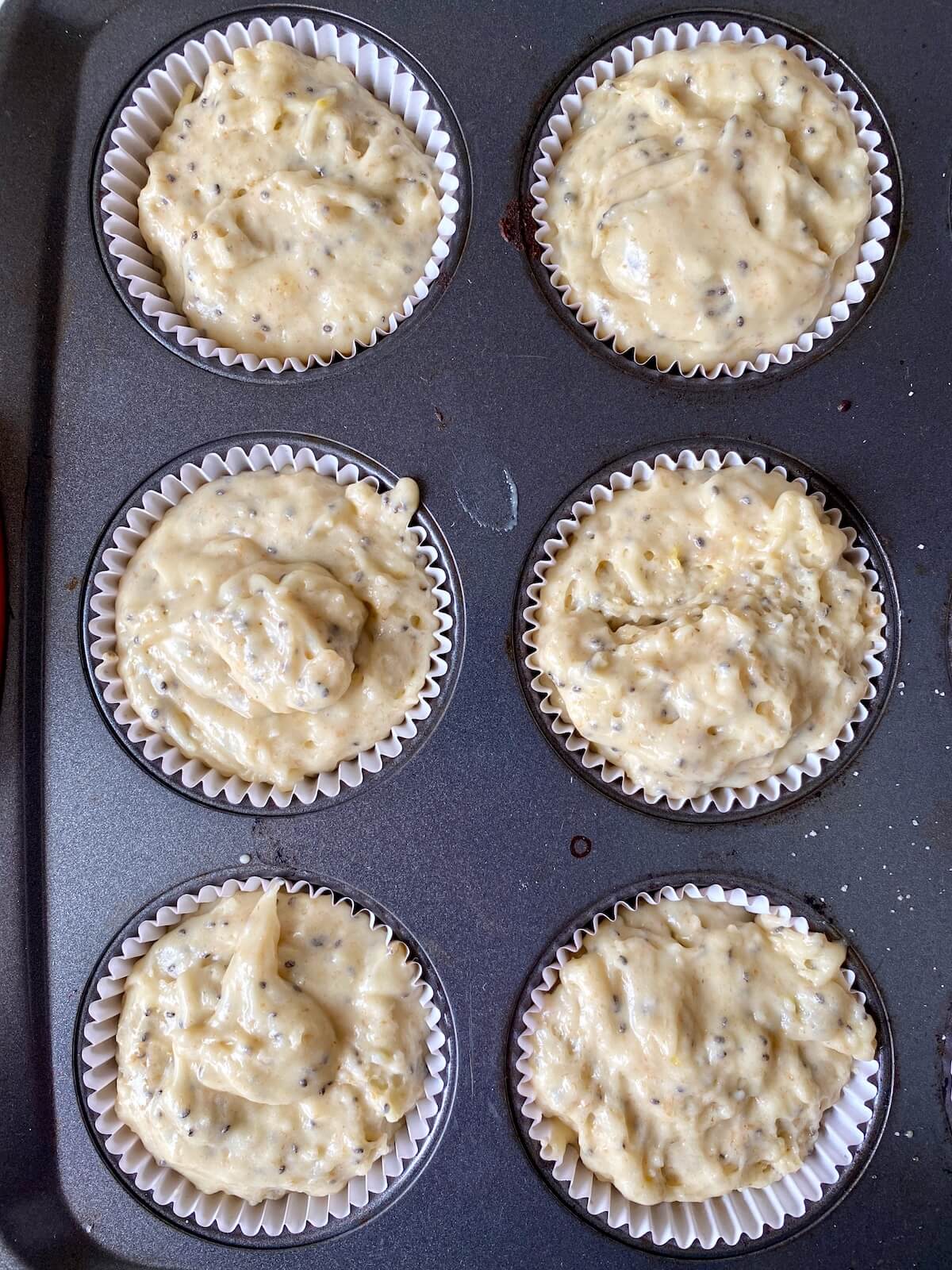 Six paper lined muffin wells filled with sourdough lemon poppyseed muffin batter.