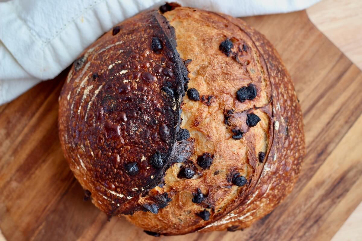 A loaf of chocolate chip sourdough bread on a wooden cutting board.