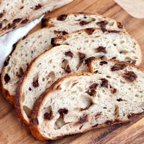 Three slices of chocolate chip sourdough bread on a wooden cutting board.