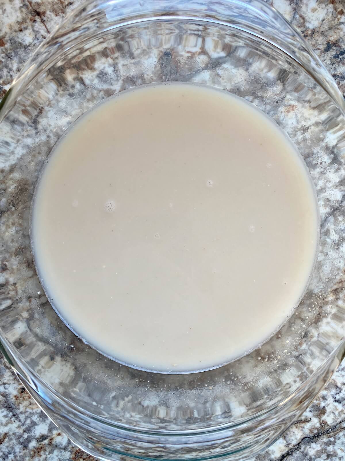 Sourdough starter and water whisked together in a glass mixing bowl.