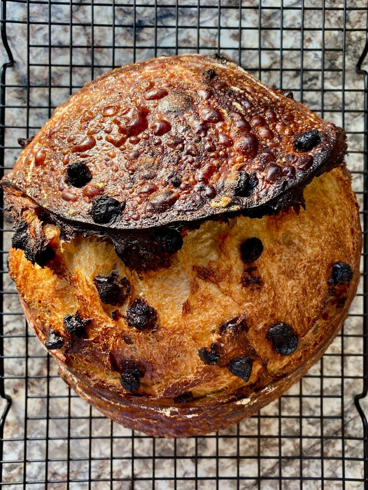 A baked loaf of sourdough chocolate chip bread on a wire cooling rack.