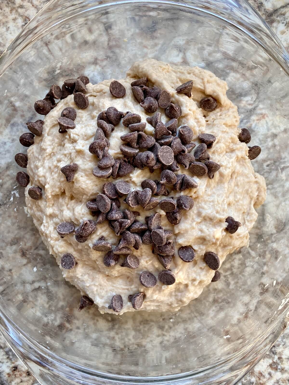 Chocolate chips sprinkled on top of the dough in a mixing bowl.