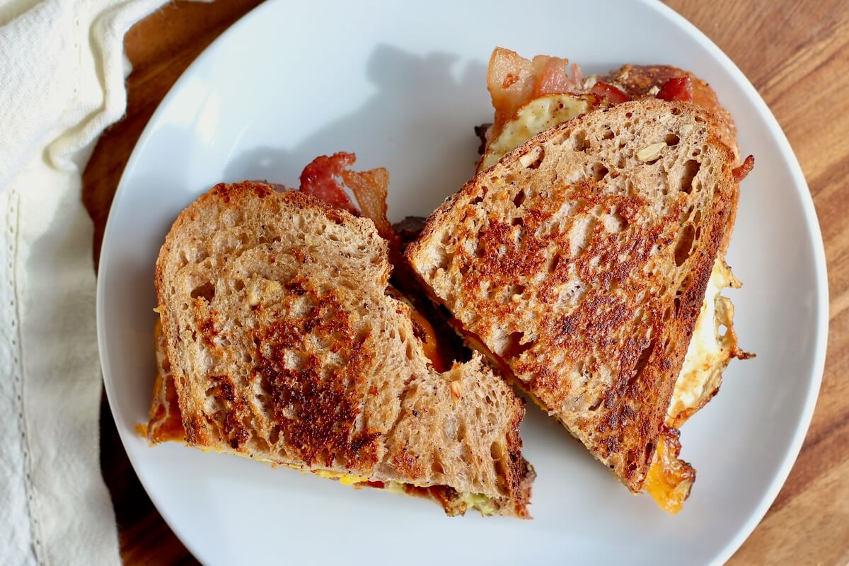 A sourdough breakfast sandwich cut in half on a small white plate.