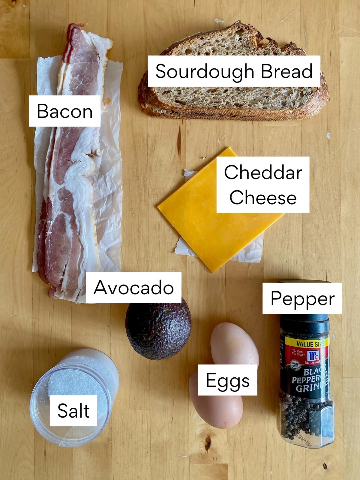 The ingredients to make a sourdough breakfast sandwich. They include sourdough bread, bacon, cheddar cheese, avocado, eggs, salt, and pepper.