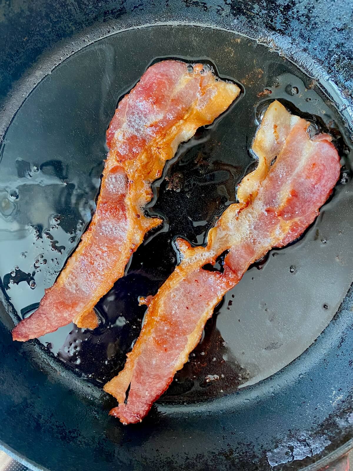 Two cooked slices of bacon in a cast iron skillet.