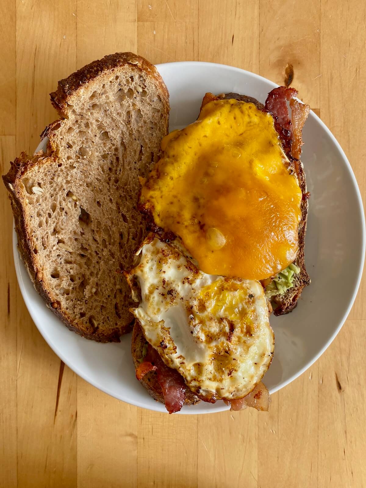 An assembled sourdough breakfast sandwich on a small white plate before topping with the top piece of sourdough bread.