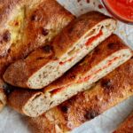 Pieces of sourdough calzone on a sheet of parchment paper next to a small bowl of marinara dipping sauce.